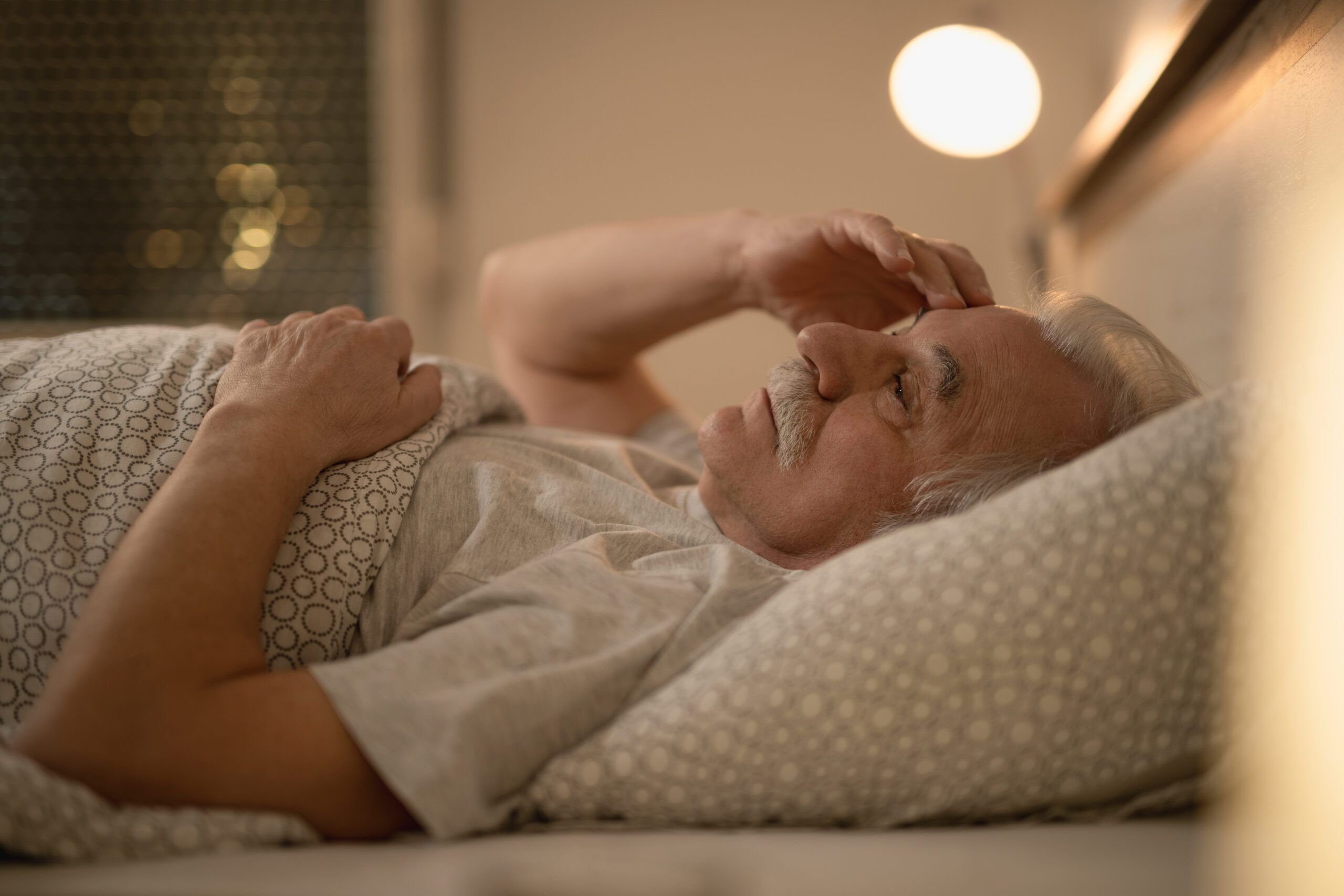 Worried senior man thinking of something while resting in bed at night.