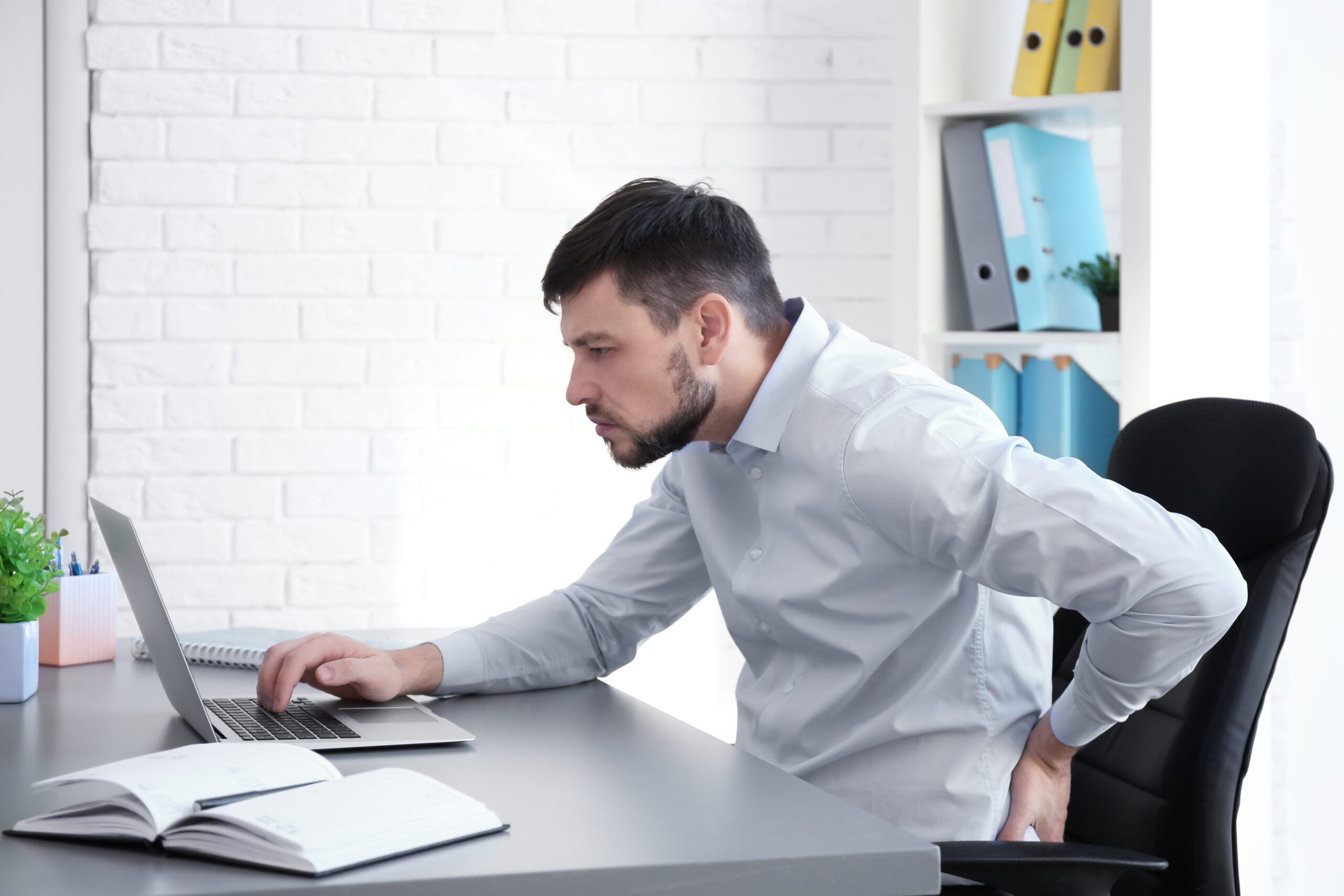 Posture concept. Man suffering from back pain while working with laptop at office