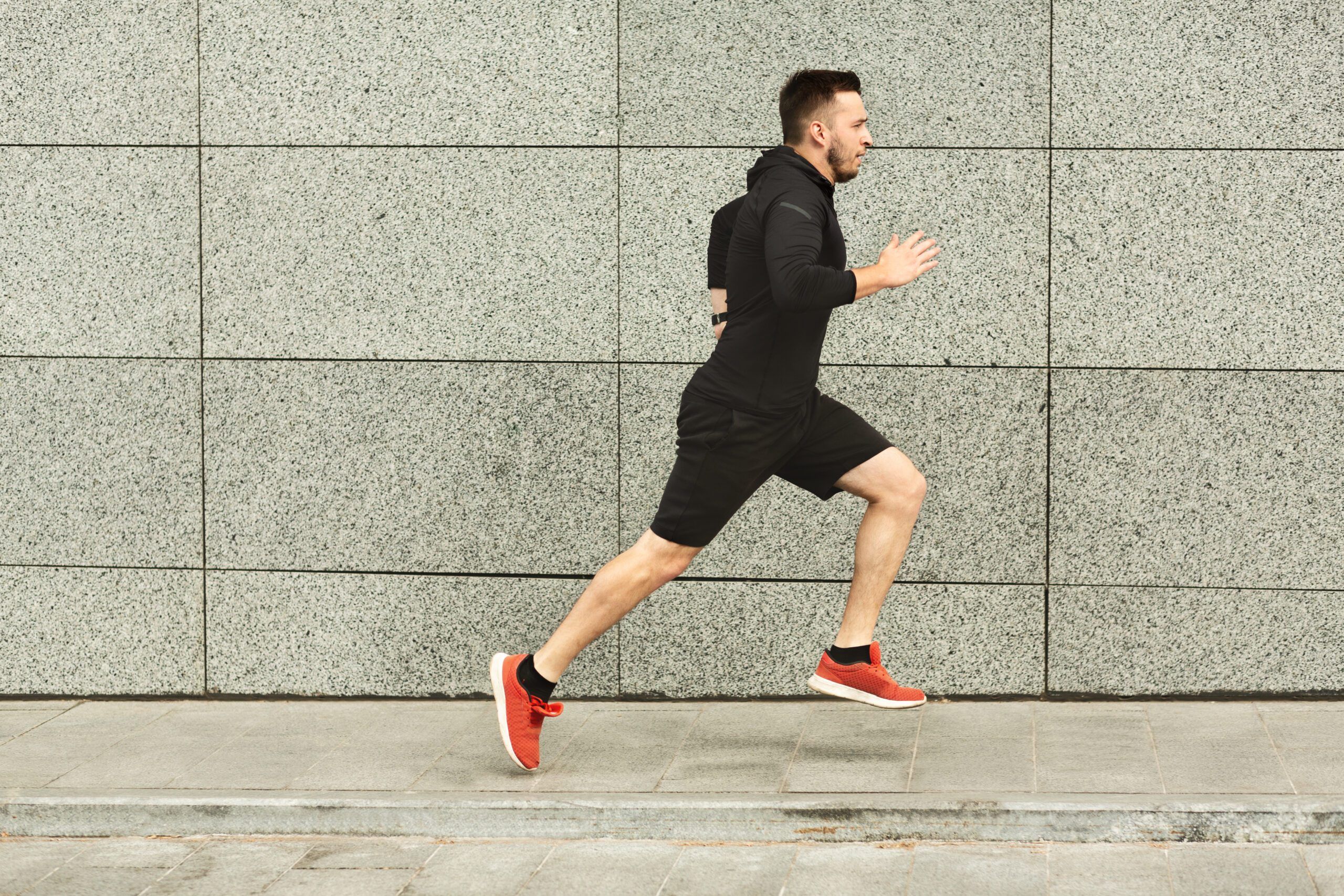 Side view of male athlete running against grey concrete wall, copy space